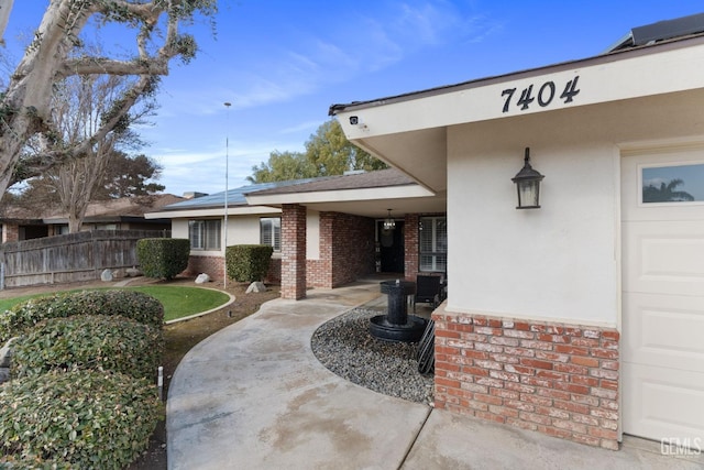 view of exterior entry featuring brick siding, fence, and stucco siding