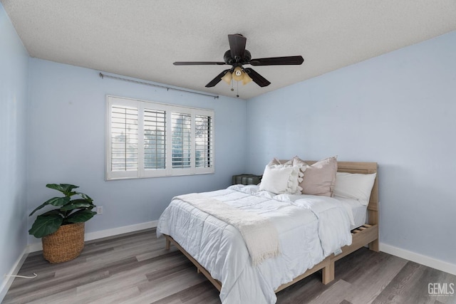 bedroom featuring ceiling fan, a textured ceiling, baseboards, and wood finished floors