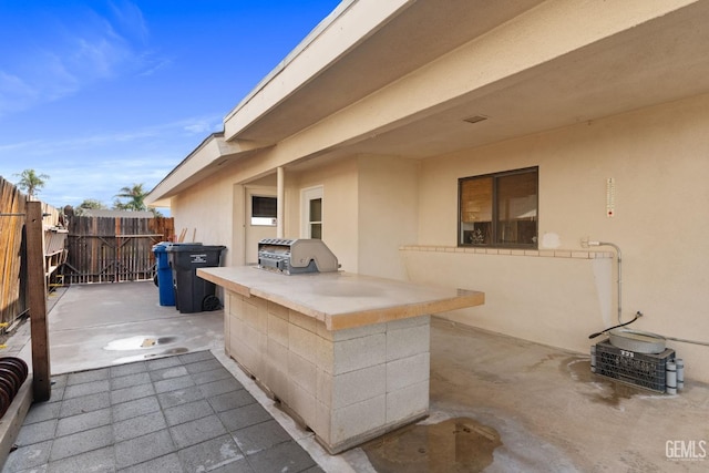 view of patio with exterior kitchen, fence, and a grill