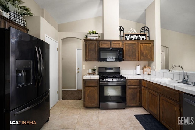 kitchen with arched walkways, tile countertops, vaulted ceiling, a sink, and black appliances