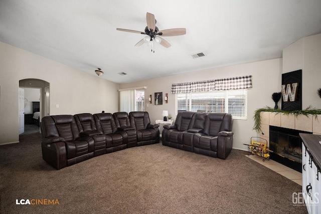 carpeted living room with arched walkways, visible vents, plenty of natural light, and a tiled fireplace