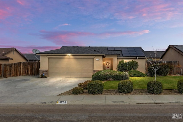 ranch-style house featuring a garage, solar panels, a lawn, fence, and stucco siding