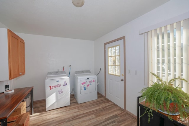 clothes washing area with washer and clothes dryer, cabinets, and light wood-type flooring