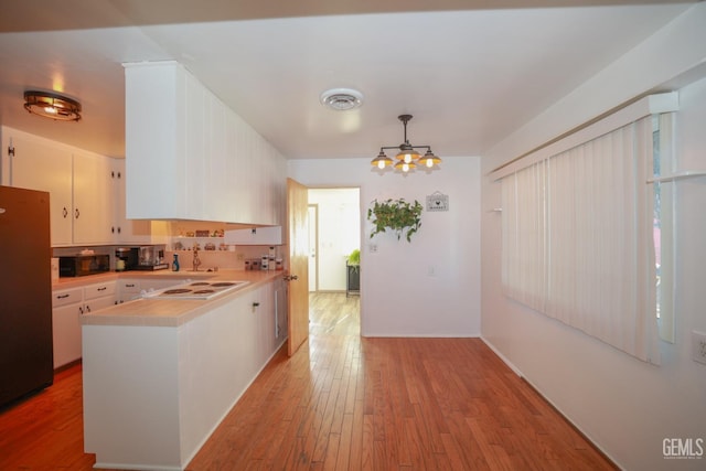 kitchen with an inviting chandelier, white cabinets, stainless steel fridge, white electric cooktop, and decorative light fixtures