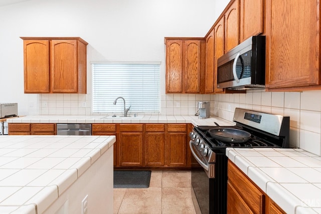 kitchen with sink, light tile patterned floors, appliances with stainless steel finishes, tile counters, and decorative backsplash