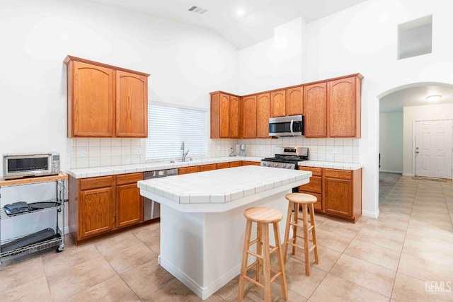 kitchen with light tile patterned flooring, tile countertops, tasteful backsplash, a center island, and stainless steel appliances