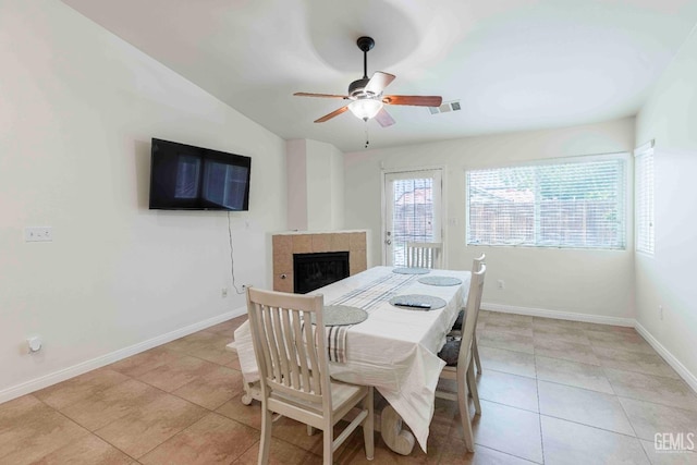 dining room with a tiled fireplace, lofted ceiling, light tile patterned floors, and ceiling fan