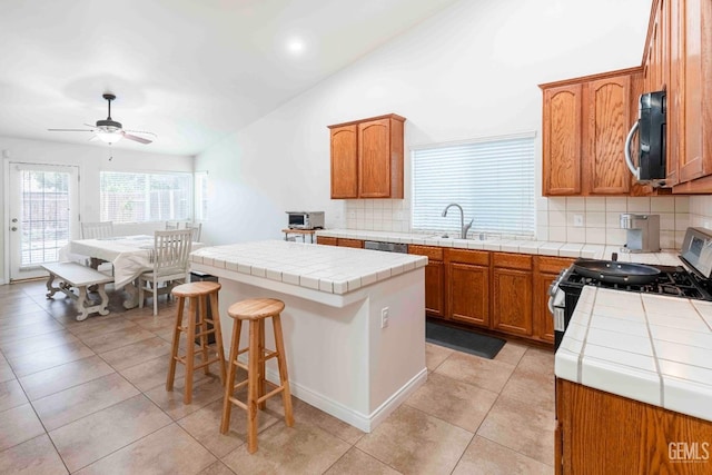 kitchen featuring a kitchen island, tile countertops, lofted ceiling, sink, and stainless steel appliances