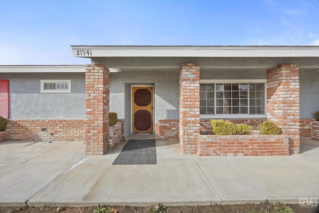 property entrance with covered porch, brick siding, and stucco siding