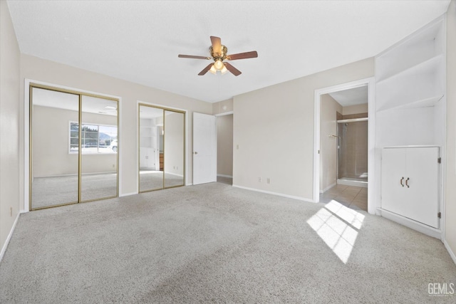 unfurnished bedroom featuring multiple closets, carpet flooring, baseboards, and ensuite bathroom