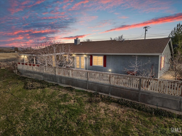 rear view of property featuring a shingled roof, a chimney, a lawn, and stucco siding