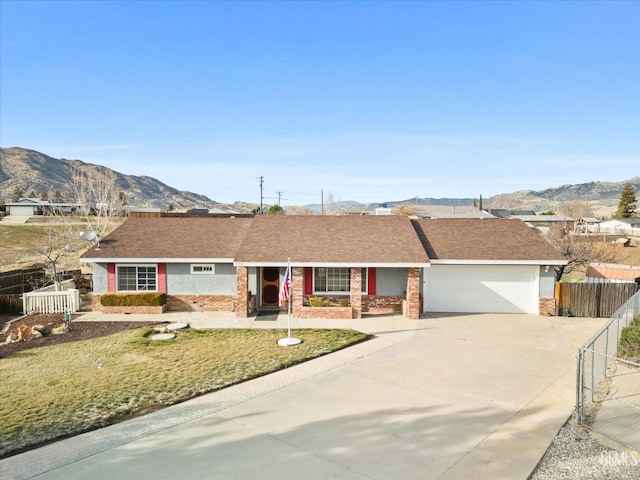 single story home featuring an attached garage, a mountain view, brick siding, fence, and driveway