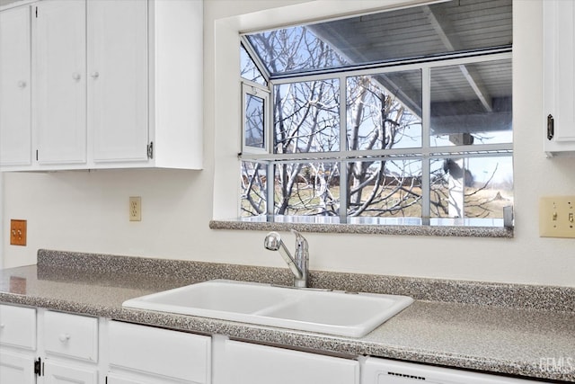 kitchen with white dishwasher, white cabinets, and a sink