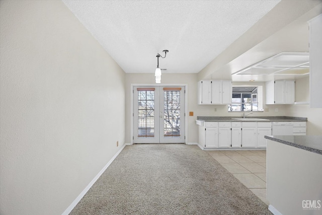 kitchen with light tile patterned floors, white dishwasher, a sink, white cabinets, and french doors