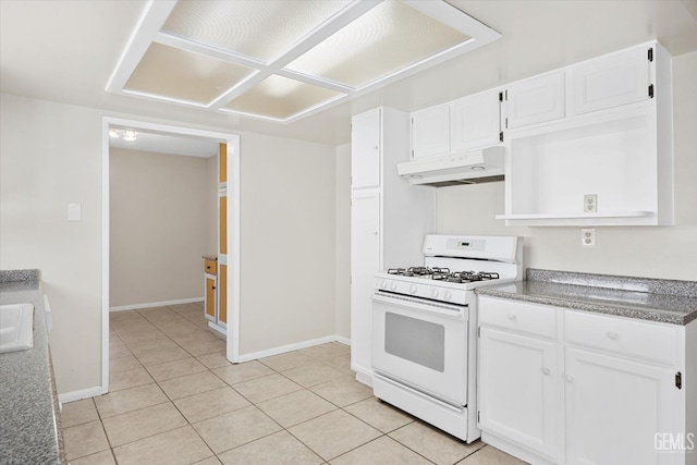 kitchen featuring white gas stove, light tile patterned flooring, under cabinet range hood, white cabinetry, and baseboards