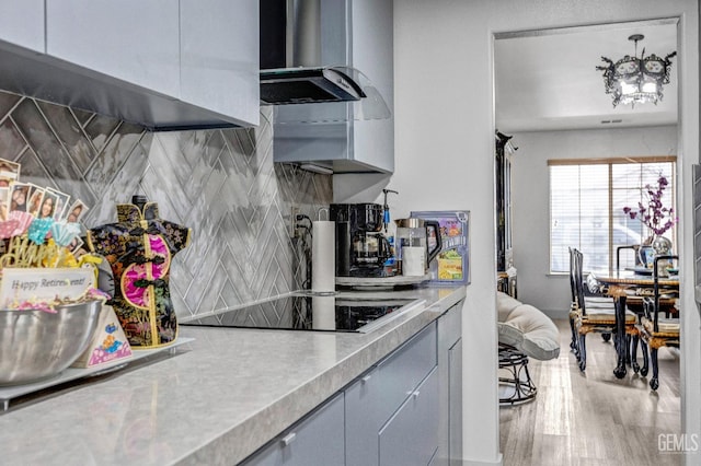 kitchen with black electric stovetop, wall chimney range hood, backsplash, and light wood-type flooring