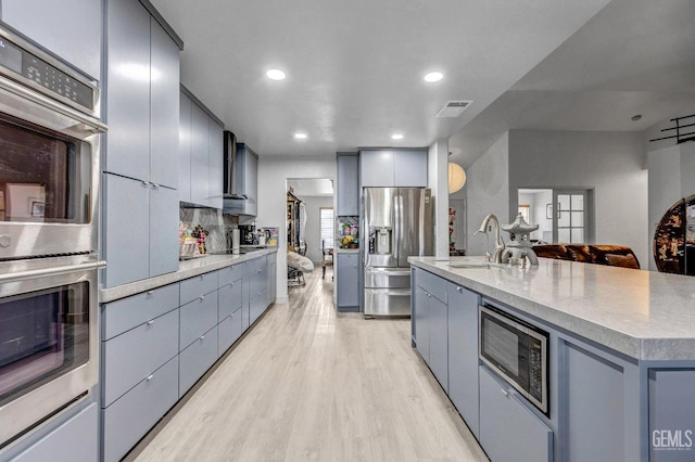 kitchen featuring sink, appliances with stainless steel finishes, tasteful backsplash, light hardwood / wood-style floors, and an island with sink