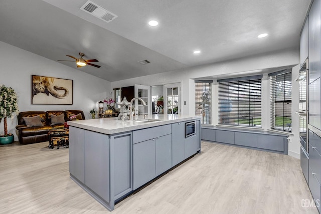 kitchen featuring lofted ceiling, sink, stainless steel microwave, light hardwood / wood-style floors, and an island with sink