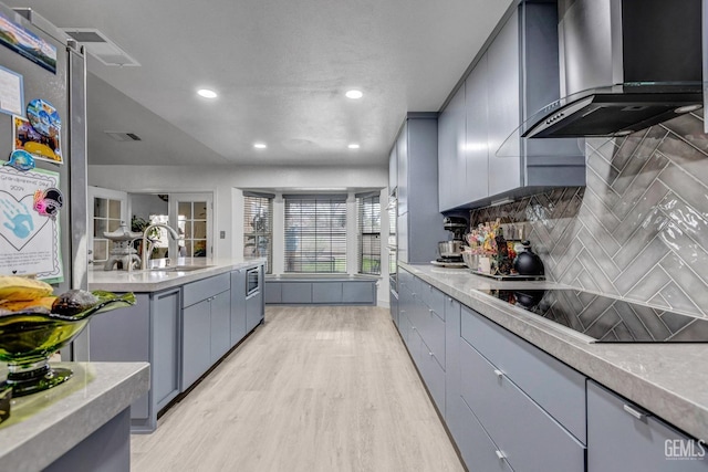 kitchen featuring sink, backsplash, light hardwood / wood-style floors, black electric cooktop, and wall chimney exhaust hood