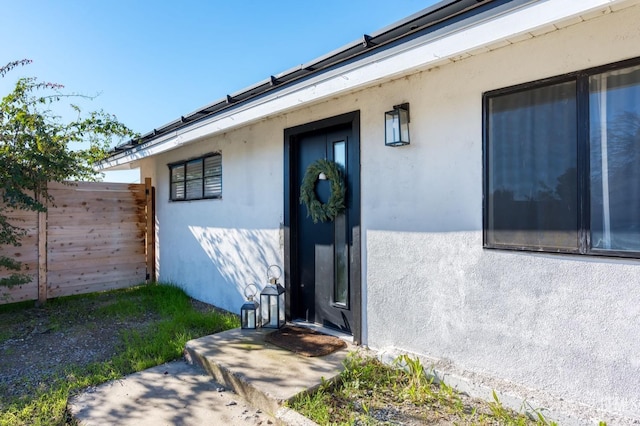 view of exterior entry featuring fence and stucco siding