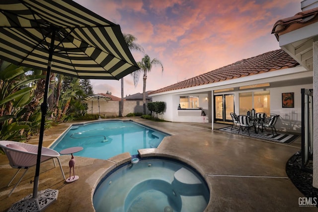 pool at dusk featuring an in ground hot tub and a patio area