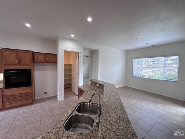 kitchen with oven, light tile patterned floors, sink, and dark stone counters