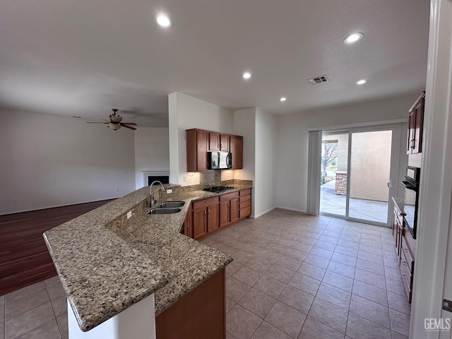 kitchen with sink, ceiling fan, light stone countertops, appliances with stainless steel finishes, and kitchen peninsula