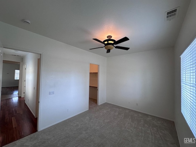 unfurnished bedroom with dark carpet, a closet, a spacious closet, and ceiling fan