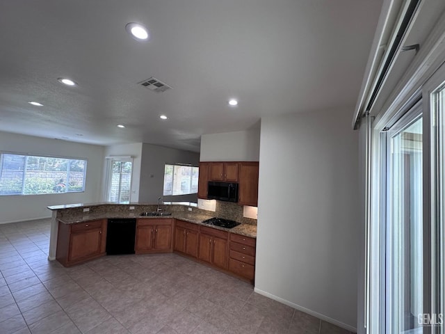 kitchen with kitchen peninsula, tasteful backsplash, black appliances, sink, and stone counters