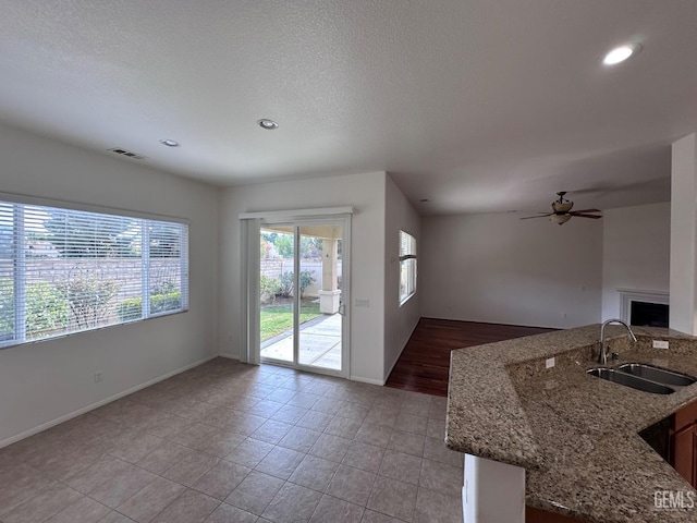 kitchen with ceiling fan, sink, a textured ceiling, stone countertops, and light tile patterned floors