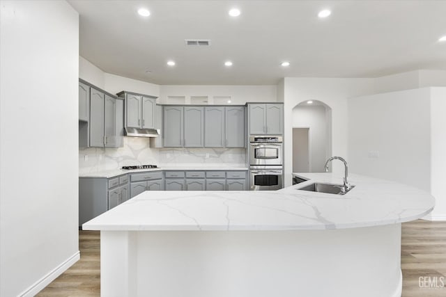 kitchen with hardwood / wood-style flooring, a kitchen island with sink, stainless steel double oven, sink, and gray cabinets