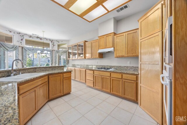 10611 Fishers Peak Dr, Bakersfield, CA 93312 - kitchen featuring under cabinet range hood, white gas cooktop, glass insert cabinets, light tile patterned flooring, and light stone countertops