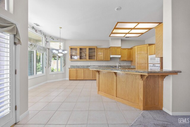 10611 Fishers Peak Dr, Bakersfield, CA 93312 - kitchen with white appliances, a breakfast bar, under cabinet range hood, glass insert cabinets, and light stone countertops