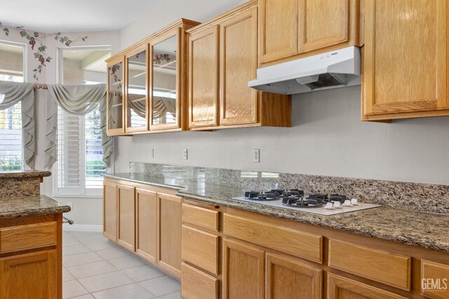10611 Fishers Peak Dr, Bakersfield, CA 93312 - kitchen with under cabinet range hood, white gas stovetop, light tile patterned floors, glass insert cabinets, and light stone countertops