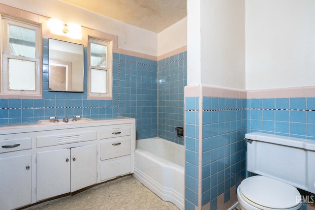 bathroom with a bathtub, tile walls, toilet, wainscoting, and vanity