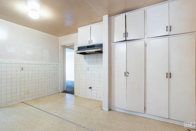 interior space with white cabinets, a wainscoted wall, light countertops, under cabinet range hood, and tile walls