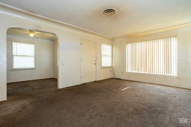 spare room featuring arched walkways, visible vents, carpet flooring, ceiling fan, and a textured ceiling