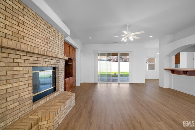 unfurnished living room featuring ceiling fan, wood-type flooring, and a fireplace