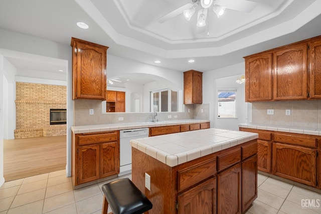 kitchen with tile counters, a tray ceiling, white dishwasher, and a center island