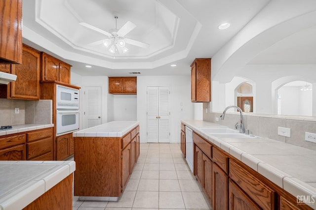 kitchen with sink, tile countertops, a center island, a raised ceiling, and white appliances