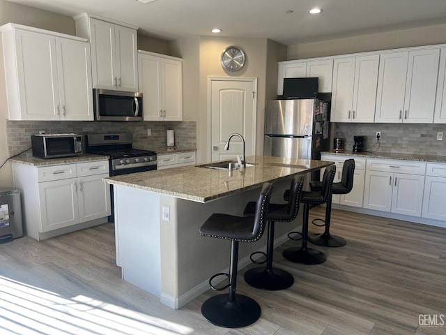 kitchen with appliances with stainless steel finishes, an island with sink, white cabinetry, and sink