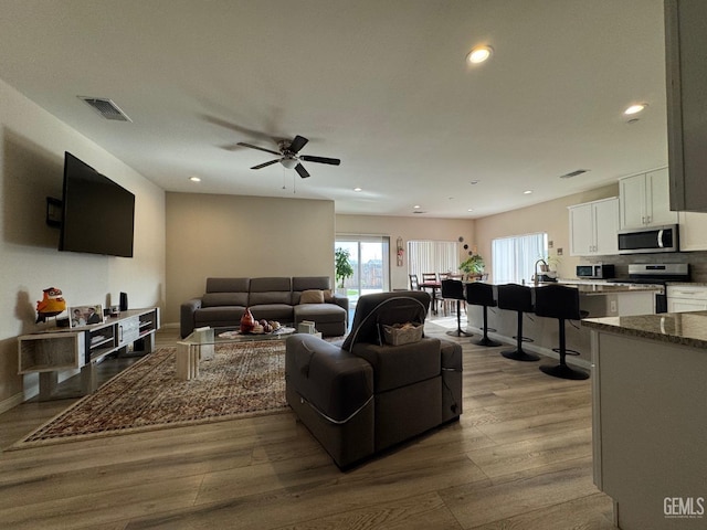 living room featuring ceiling fan, light hardwood / wood-style flooring, and sink