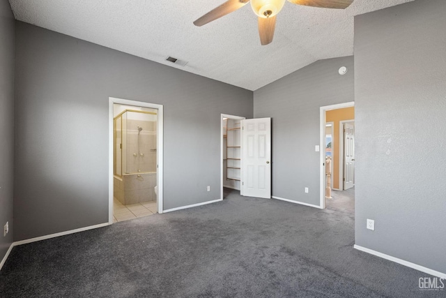 unfurnished bedroom featuring lofted ceiling, ceiling fan, ensuite bathroom, carpet, and a textured ceiling