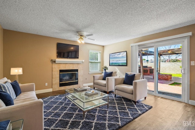 living room with ceiling fan, wood-type flooring, a fireplace, and a textured ceiling