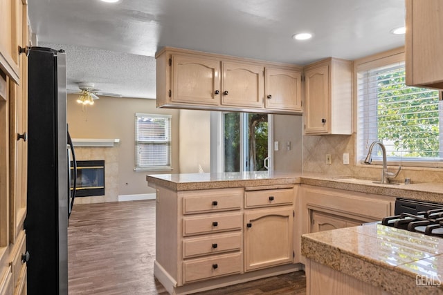 kitchen with sink, stainless steel refrigerator, a tiled fireplace, decorative backsplash, and kitchen peninsula