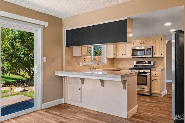 kitchen with a kitchen bar, light hardwood / wood-style flooring, kitchen peninsula, stainless steel appliances, and decorative backsplash