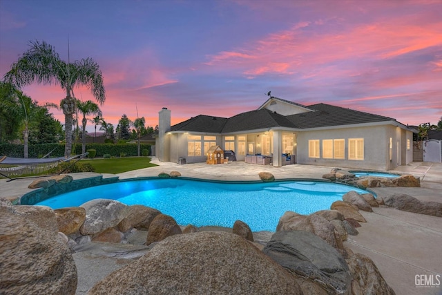 pool at dusk featuring a patio area and an in ground hot tub