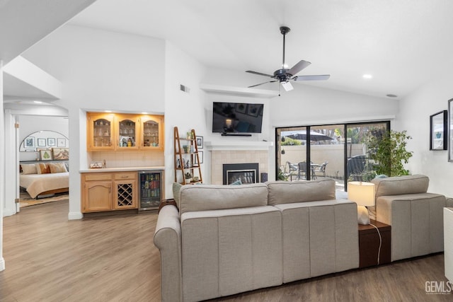 living room featuring light wood-type flooring, a fireplace, indoor bar, ceiling fan, and beverage cooler