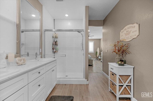 ensuite bathroom featuring wood finish floors, double vanity, a shower stall, and a sink