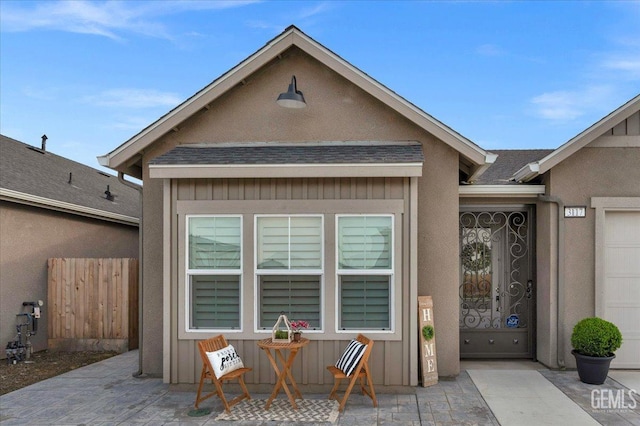 property entrance featuring stucco siding, a shingled roof, and fence